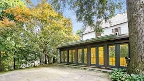 A covered patio area with stone flooring, surrounded by trees and a building with large windows.