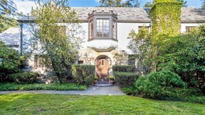 A traditional stone house with a central entrance, surrounded by well-maintained hedges and a grassy lawn.