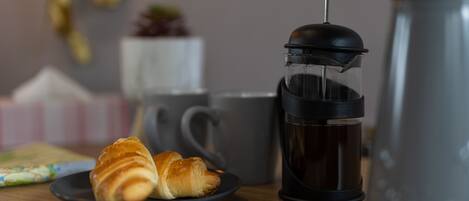 A coffee maker, a plate with croissants, and a mug on a wooden table.