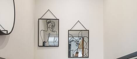 A modern bathroom with a white sink, toilet, and shower. There are two framed artworks on the wall.