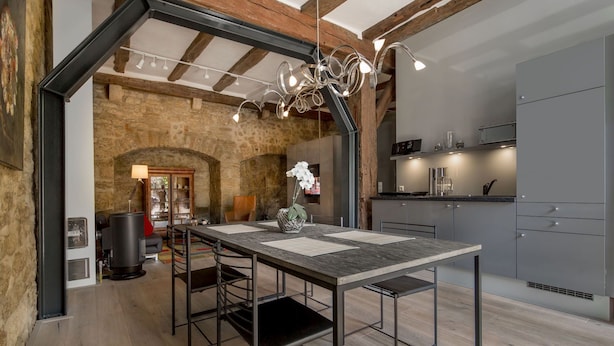 A modern kitchen with a central island, built-in appliances, and a stone archway leading to a dining area.