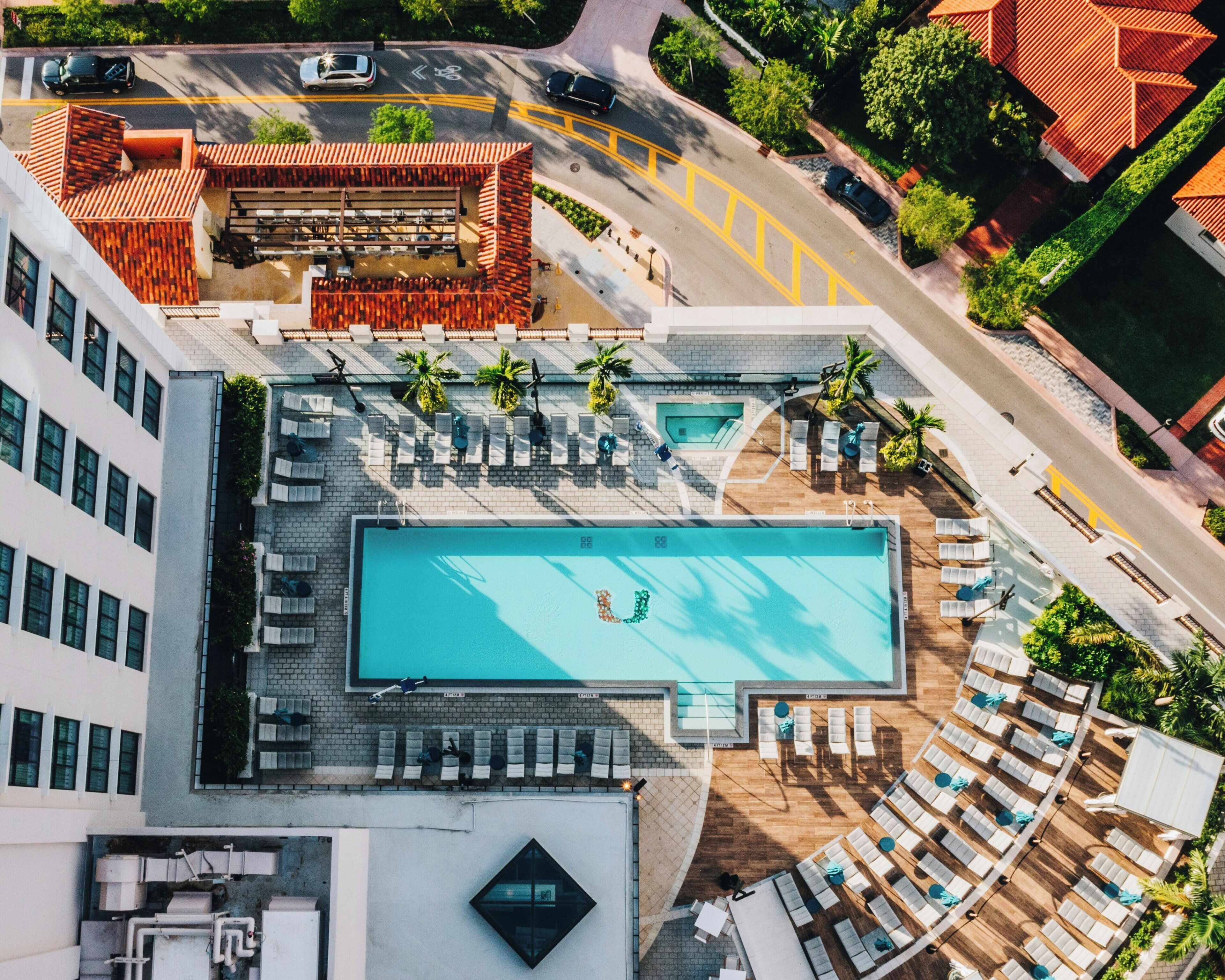 An aerial view of a rooftop swimming pool with sun loungers and a small bridge connecting to a parking area.