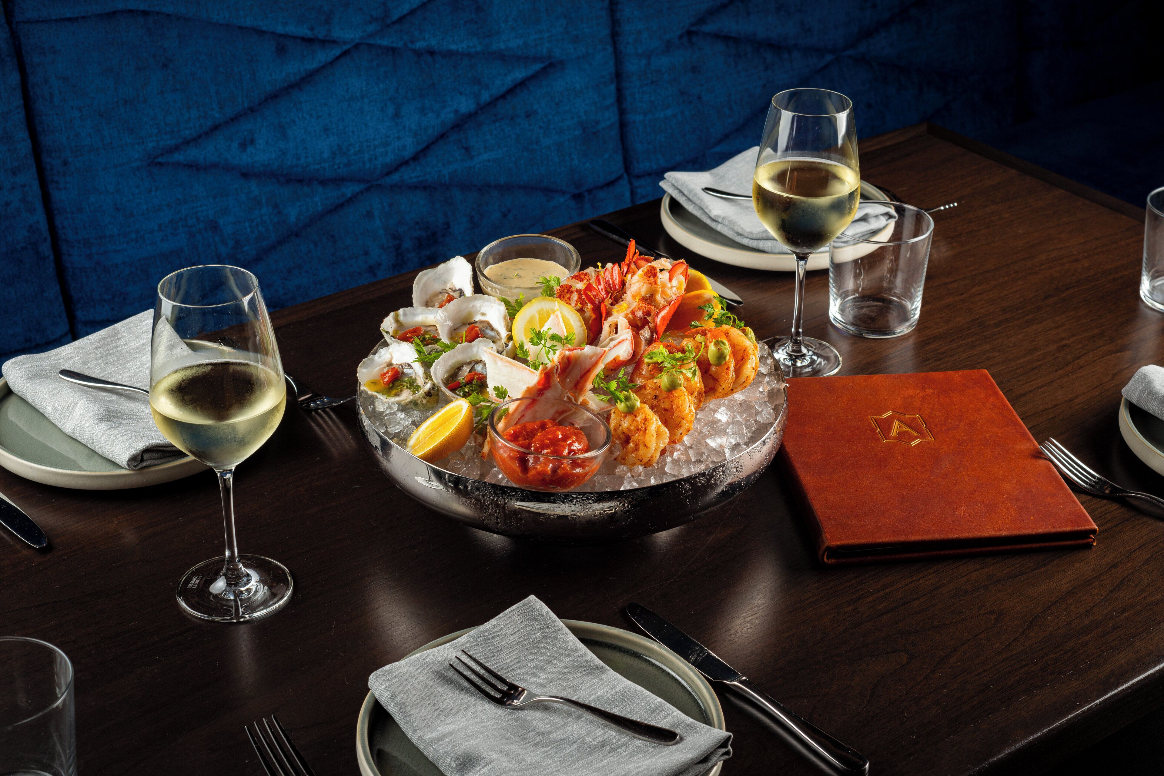 Uma mesa de jantar com frutos do mar, copos de vinho e um cardápio.