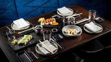 Una mesa de comedor dispuesta con diversos platos, palillos, vasos y una servilleta.
