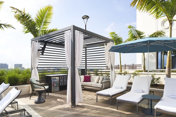 Area lounge sulla terrazza con poltrone, un piccolo bar e un pergolato con tende bianche.