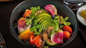 A bowl of salad with various vegetables and a glass of water on a table.