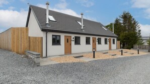 A modern building with a sloped roof, multiple windows, and a wooden fence. - Sycamore Cottage (Tenby)