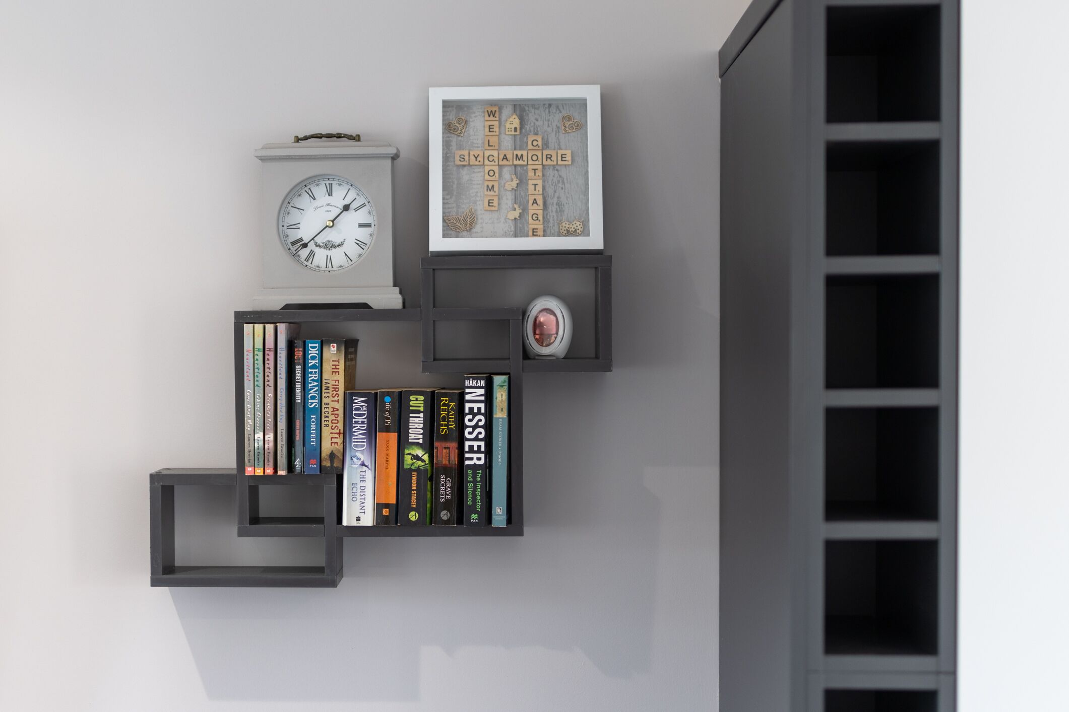 Ein an der Wand befestigtes Bücherregal mit Büchern, einer Uhr und einem gerahmten Willkommensschild.