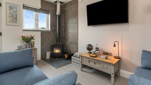 A modern living room with a fireplace, a flat-screen TV, and a cozy seating area. - Sycamore Cottage (Tenby)