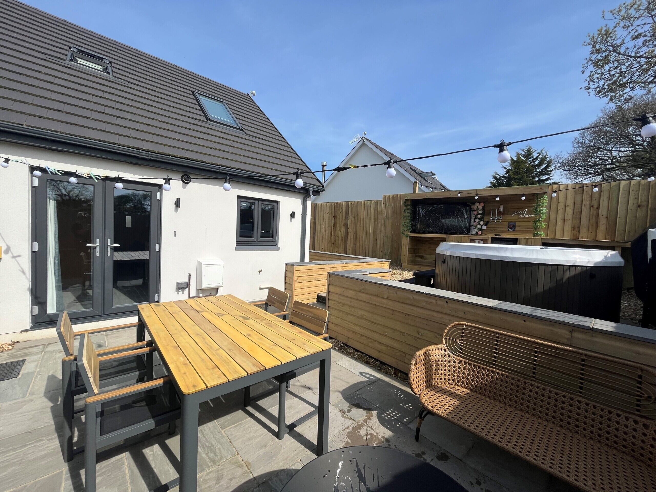 A patio area with a wooden table and chairs, a hot tub, and a wooden fence.