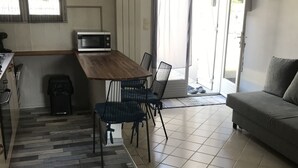 A modern kitchen with a wooden table, black chairs, a microwave, and a trash bin. - Cosy semi-detached house, terrace 800m from the swimming pool (Lanton)