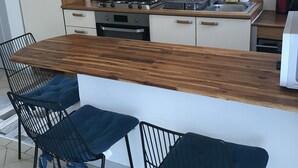 A modern kitchen with a central island, wooden cabinets, and black chairs with blue cushions. - Cosy semi-detached house, terrace 800m from the swimming pool (Lanton)