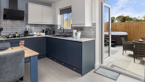A modern kitchen with a central island, built-in appliances, and a dining area with outdoor seating. - Birch Cottage (Tenby)
