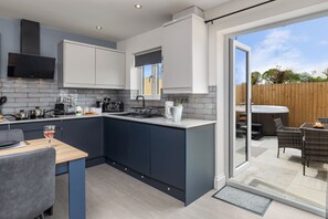 A modern kitchen with a central island, built-in appliances, and a dining area with outdoor seating. - Birch Cottage (Tenby)