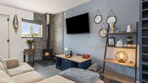 A modern living room with a fireplace, a TV mounted on the wall, and a cozy seating area with a sofa and armchairs. - Birch Cottage (Tenby)