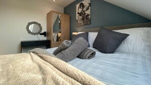 A bedroom with a bed, a nightstand, a mirror, and a painting on the wall. - Birch Cottage (Tenby)