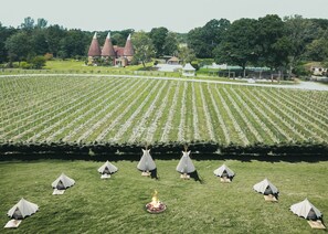 A large field with tents and a central fire pit, surrounded by a building with conical roofs. - Oastbrook Glamping (Robertsbridge)