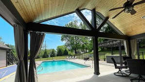 Un espacio al aire libre techado con piscina, techo de madera y mobiliario exterior.
