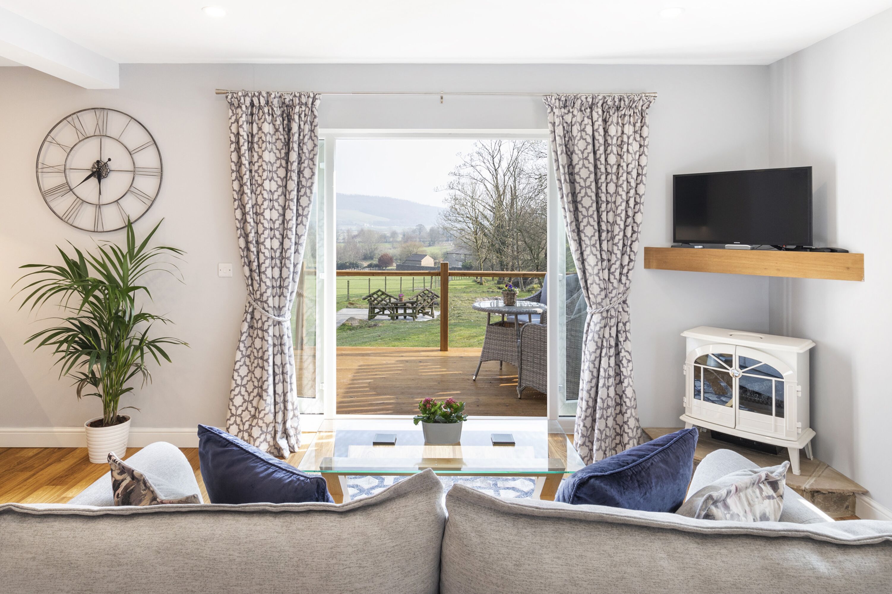 A living room with a sofa, a coffee table, a TV, a plant, and a view of the outdoors.