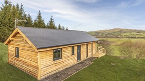 A wooden cabin with a sloped roof, a small porch, and a view of the surrounding landscape. - Throstle Nest Farm Lodges (Skipton)