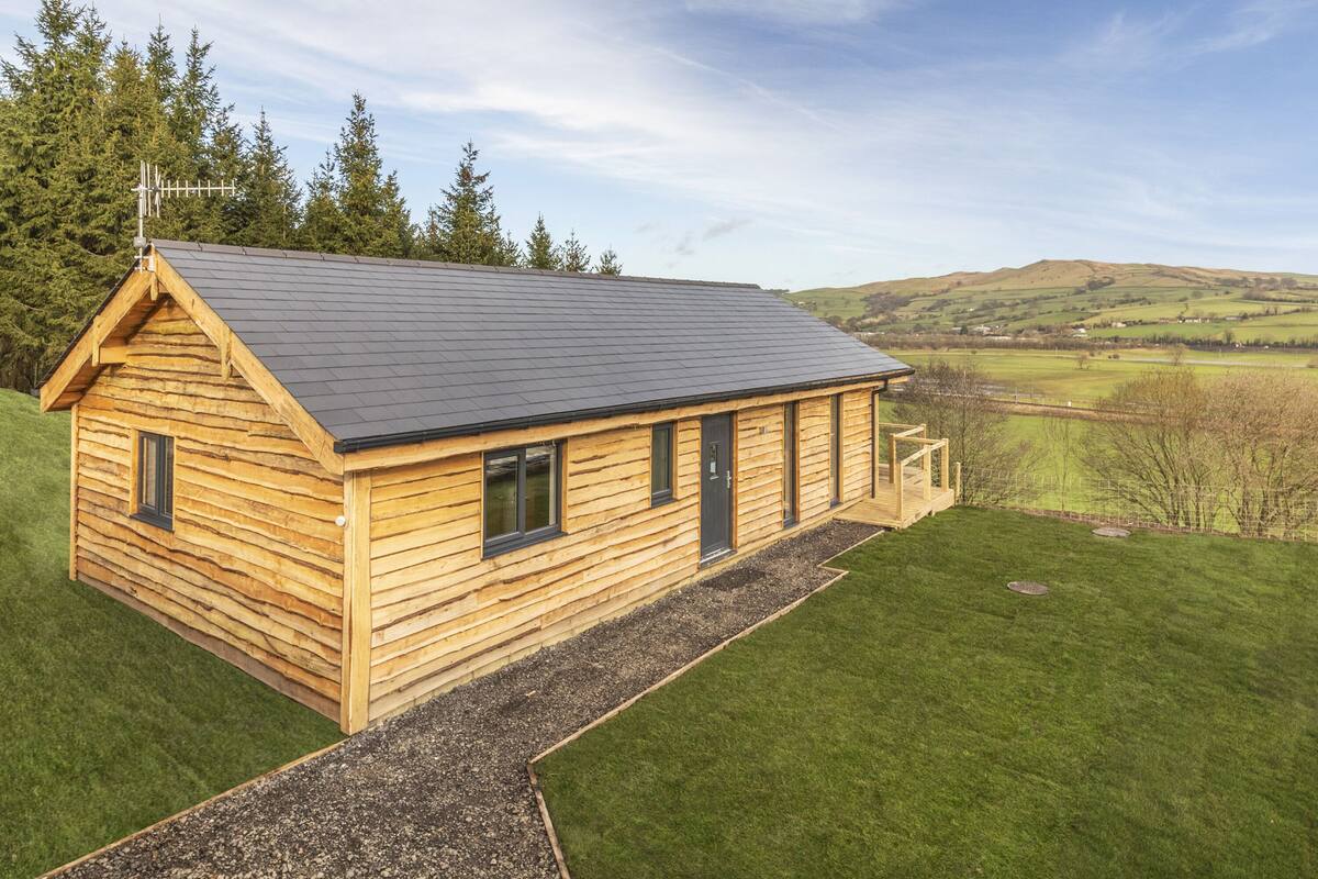 A wooden cabin with a sloped roof, a small porch, and a view of the surrounding landscape.