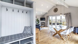 A modern living room with a glass dining table, white chairs, a sofa, and a bench with storage. - Throstle Nest Farm Lodges (Skipton)