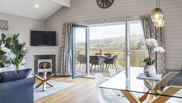 A modern living room with a fireplace, a TV, and a glass table with chairs. - Throstle Nest Farm Lodges (Skipton)