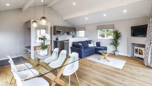 A modern living room with a glass dining table, white chairs, a blue sofa, and a fireplace. - Throstle Nest Farm Lodges (Skipton)