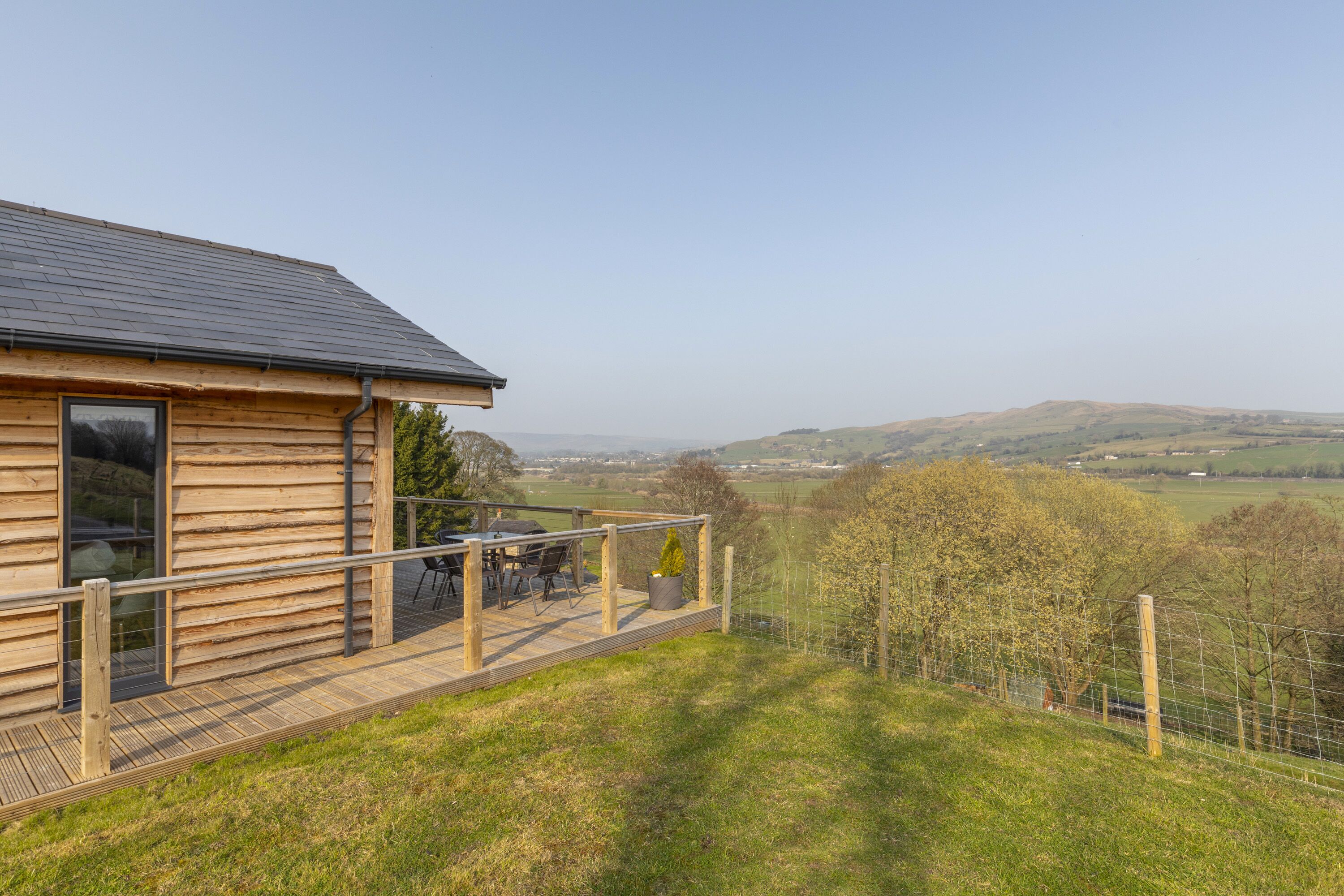 A wooden cabin with a deck, large windows, and a view of rolling hills.