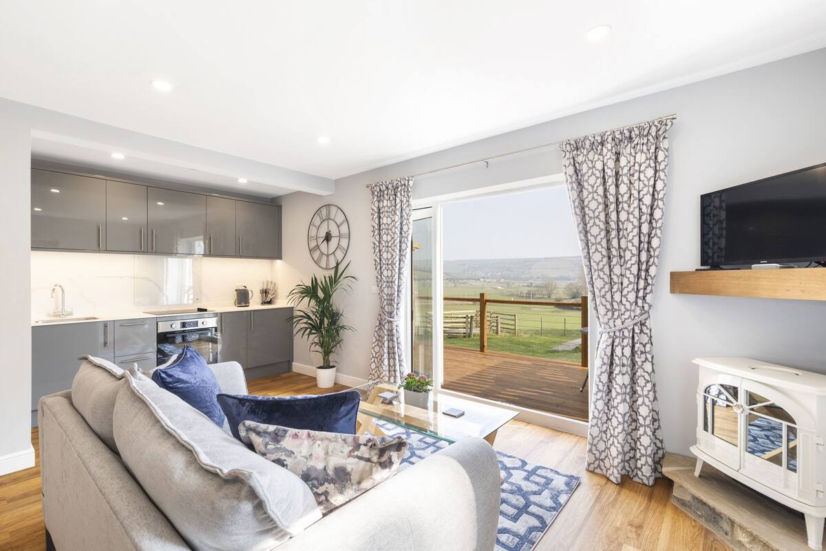 A modern living room with a sofa, a television, and a view of a balcony with a wooden deck.