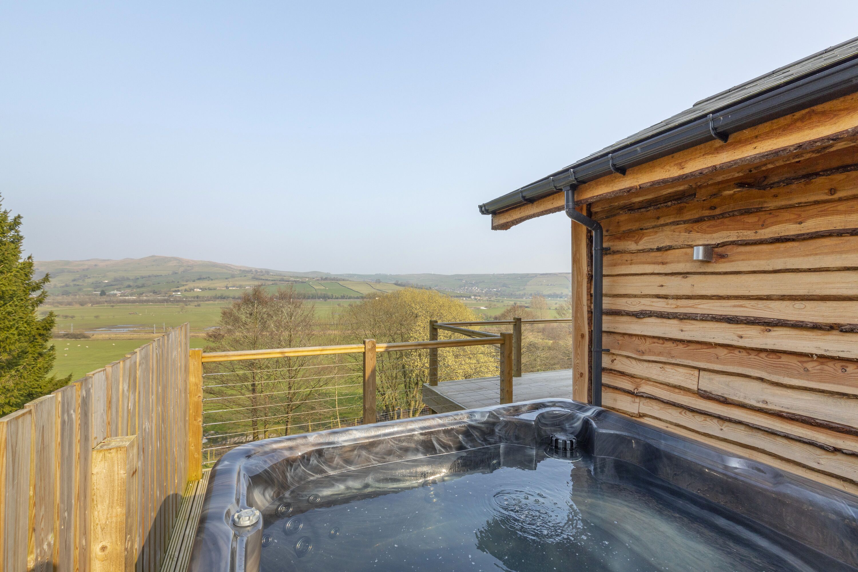 A hot tub on a wooden deck with a view of rolling hills.