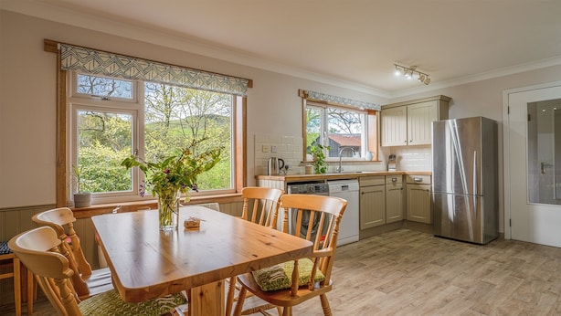 A kitchen with wooden cabinets, a stainless steel refrigerator, and a dining table with chairs. - Keppoch Cottage (Crieff)