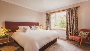 A bedroom with a large bed, a nightstand with a lamp, a chair, and a window with curtains. - Keppoch Cottage (Crieff)