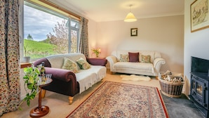 A cozy living room with a sofa, armchair, and a fireplace. - Keppoch Cottage (Crieff)