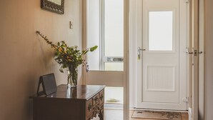 A hallway with a wooden table, a vase with flowers, a mirror, and a door leading to another room. - Keppoch Cottage (Crieff)