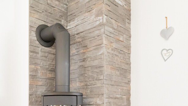 A modern room with a stone accent wall, a glass-top table, a wicker basket, and a fireplace with a chimney. - Beautiful newly renovated vacation apartment in a quiet location (Wald-Michelbach)