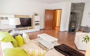 A modern living room with a flat-screen TV, a white sofa with green and yellow cushions, a white coffee table, and a stone fireplace.