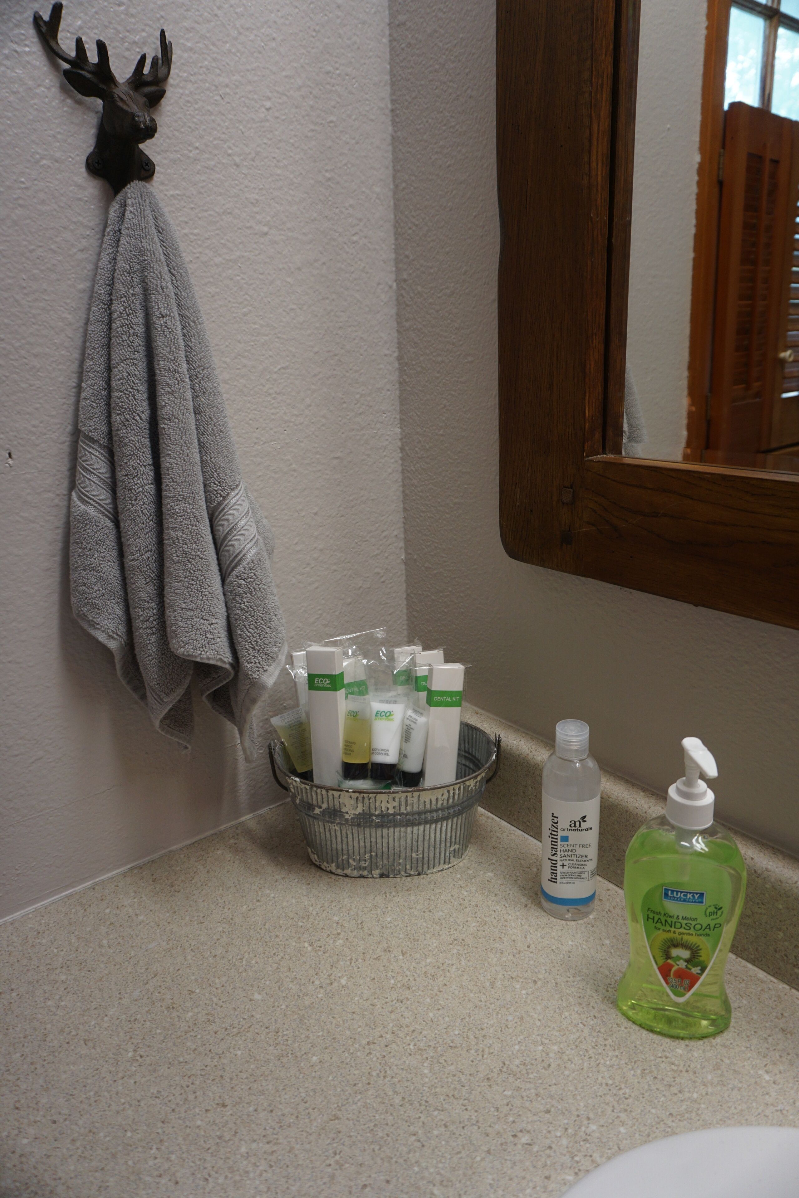 A bathroom with a towel rack, a basket of toiletries, and a bottle of hand soap.