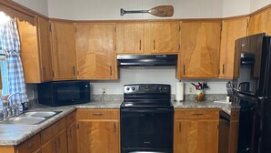 A kitchen with wooden cabinets, a black stove, a microwave, and a refrigerator. - Cozy house  close to public land areas for recreation! (West Mineral)
