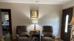 A living room with two armchairs, a small table with a lamp, a framed picture on the wall, and a door with a window. - Cozy house  close to public land areas for recreation! (West Mineral)