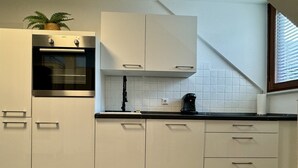 Une cuisine moderne avec des armoires blanches, un four encastré et une machine à café posée sur le plan de travail.