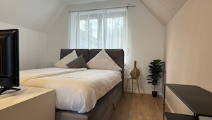 Une chambre à coucher avec un lit, une télévision, une petite table, une plante et une fenêtre avec des rideaux.