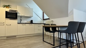 Une cuisine moderne avec des meubles blancs, un four noir et une machine à café. On y trouve également un coin repas avec une table et deux chaises.