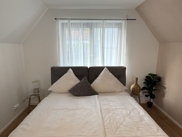 A bedroom with a bed, two pillows, a bedside table, a lamp, and a potted plant. - Ferienhaus Möhrle 6 (Ueberlingen)