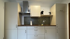 A modern kitchen with grey cabinets, a stainless steel range hood, a coffee maker, and a kettle on the countertop.