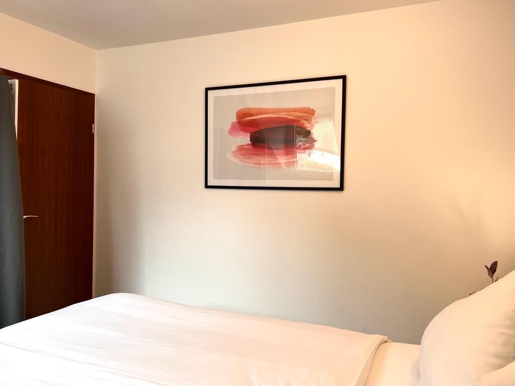 A bedroom with a bed, a framed abstract painting, and a wooden door.