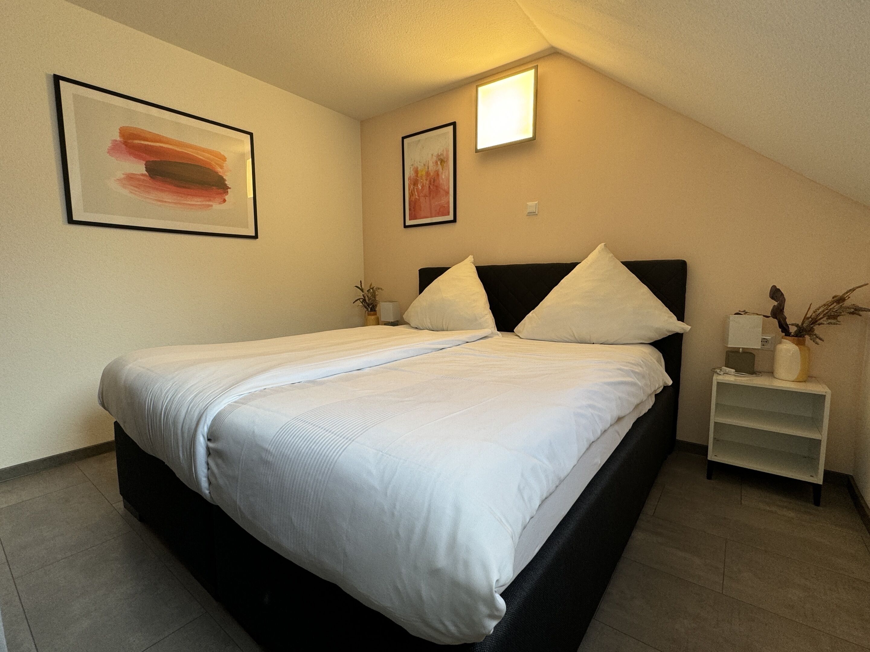 Een keurig opgemaakt slaapkamer met een bed, nachtkastjes en wanddecoratie.