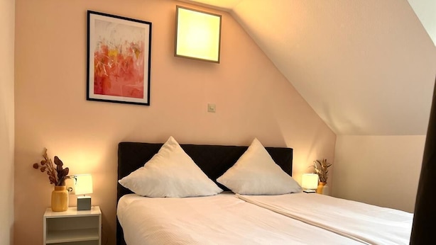 A bedroom with a bed, two bedside tables, a nightstand, a framed picture, and a wall-mounted light.