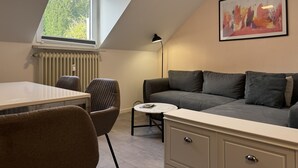 A modern, well-lit room with a dining table, chairs, a sofa, a small round table, and a radiator.