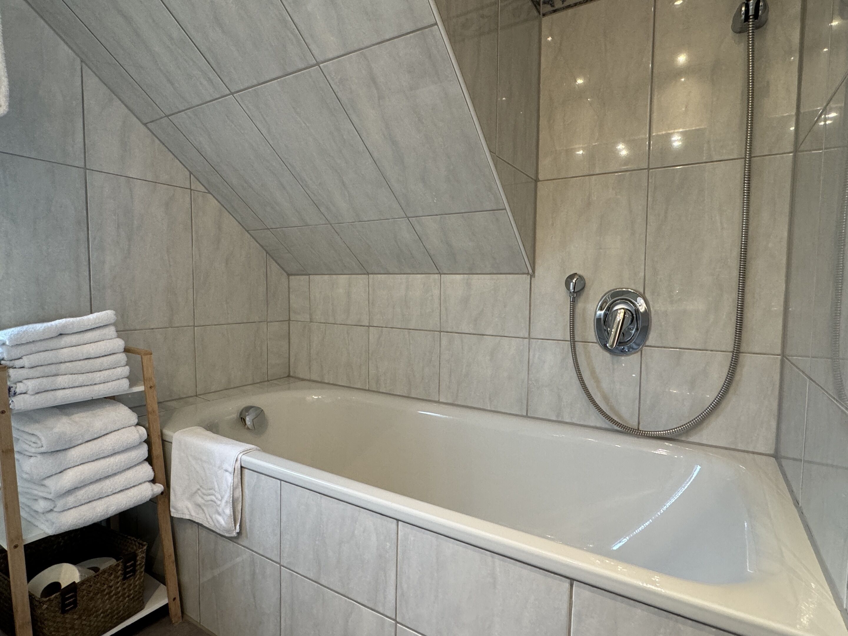 Un baño moderno con una bañera independiente, un cabezal de ducha y un perchero con toallas ordenadas.